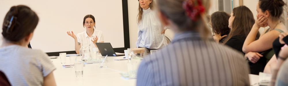 Person pratar inför grupp vid ett bord