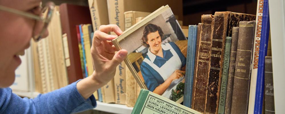 Person tar ut en kokbok ur en hylla i arkivet