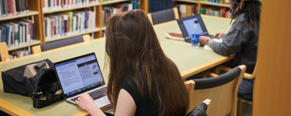 Två studenter som sitter och pluggar vid stora bordet inne i KvinnSams bibliotek